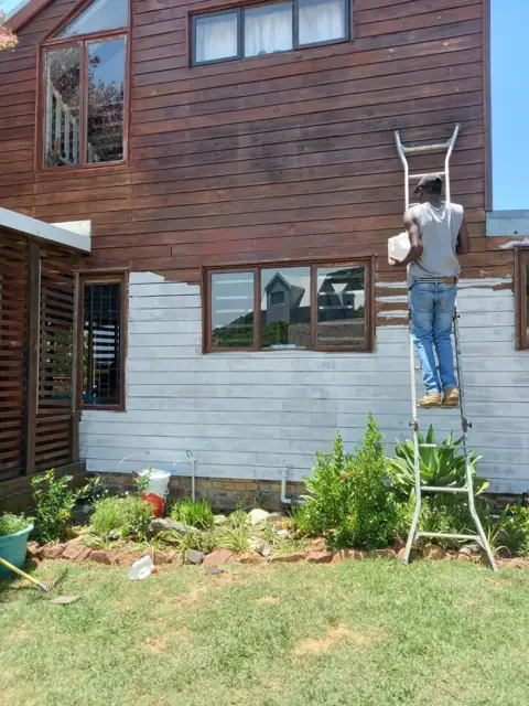 Painter on a ladder priming timber cladding