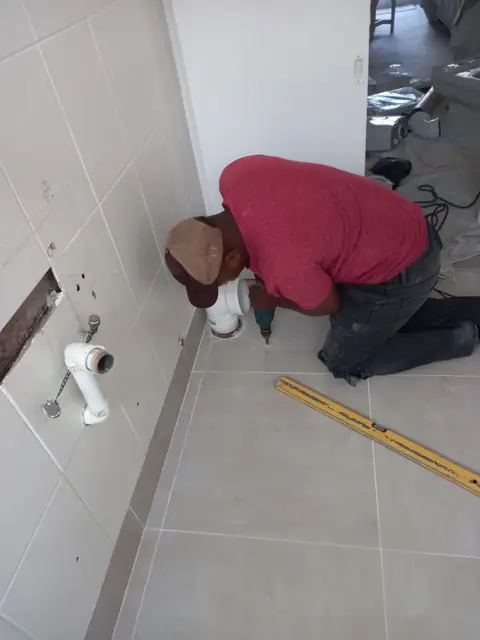 Plumber working on floor-level pipework in a bathroom