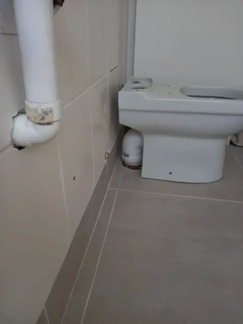 Toilet with exposed soil pipe in a tiled bathroom