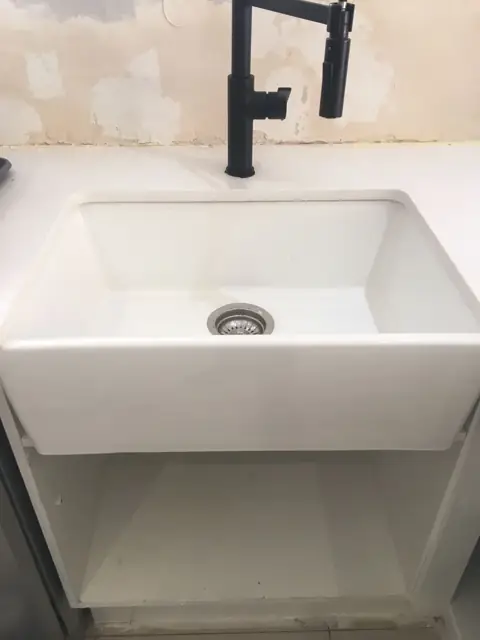 Butler sink fitted with black mixer tap, wall stripped