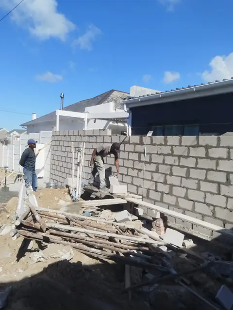 Workers building a grey block boundary wall