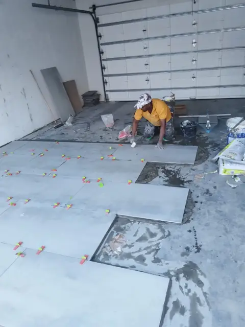 Worker laying large grey floor tiles in a garage