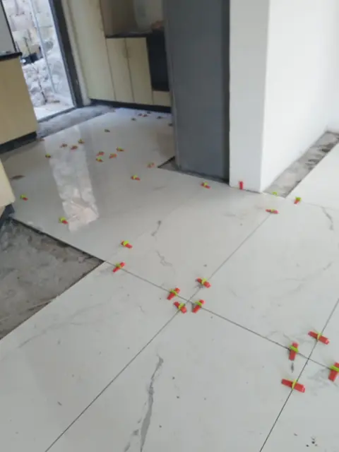 Polished marble-look floor tiles with levelling clips at a doorway