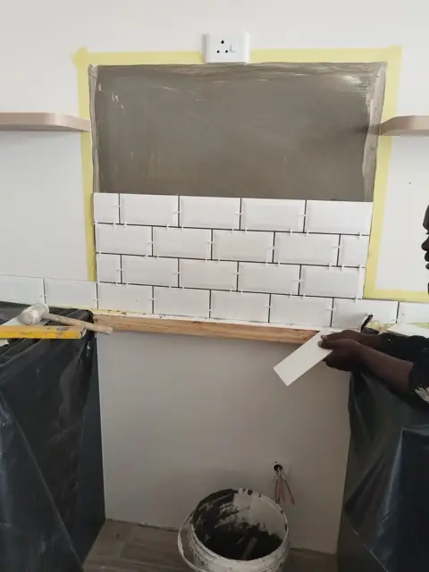 Subway-tile splashback being installed over taped adhesive bed