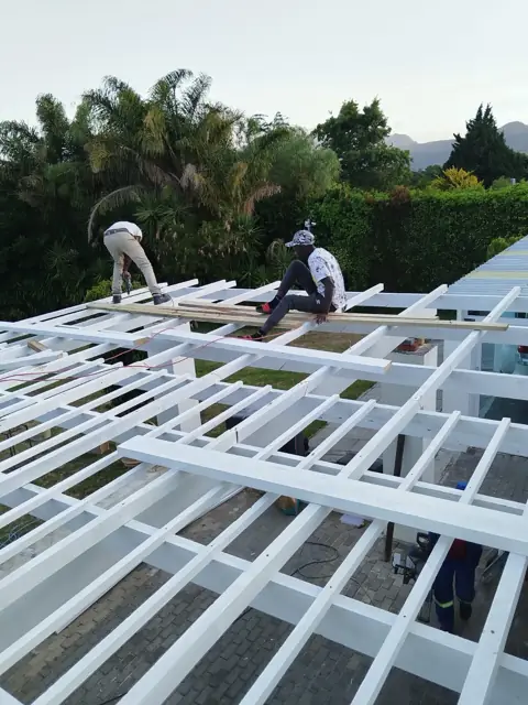 Workers assembling a white-painted roof beam grid