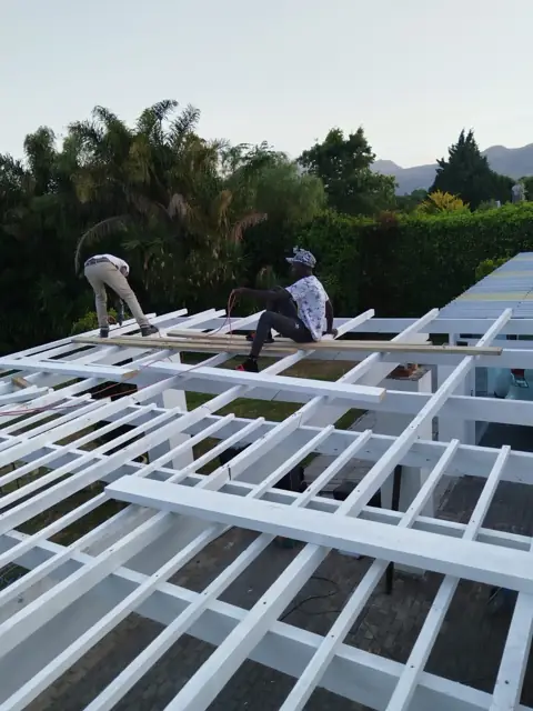 Two workers on a white-painted flat roof beam grid