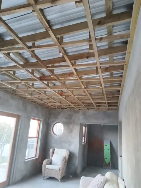 Timber ceiling brandering grid inside a room under a corrugated roof; alt roofing