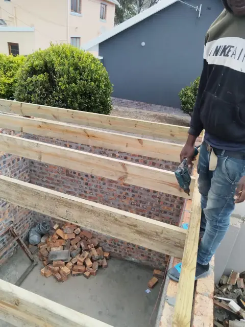 Worker building a timber pergola structure above a brick wall