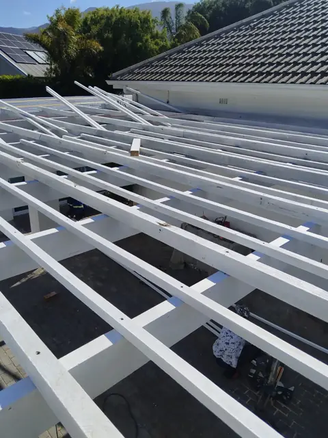 White-painted roof grid over dark sheeting, viewed down the slope