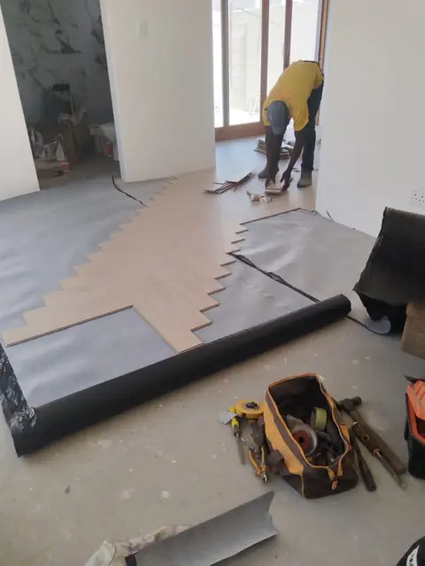 Worker laying underlay and new flooring in a room with tools