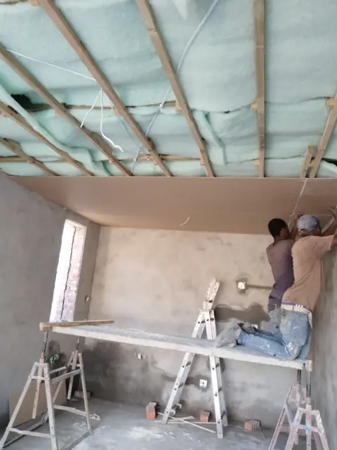 Team plastering interior walls on scaffold boards