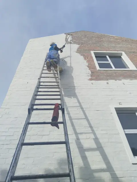 Painter on ladder painting exterior gable wall