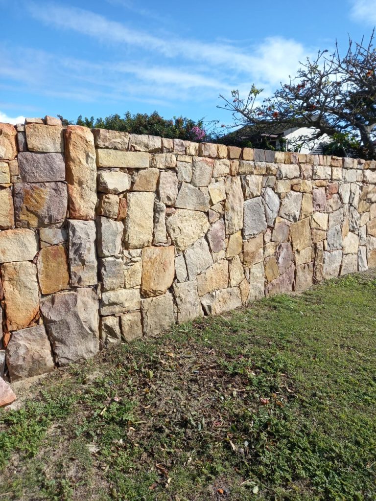 Long natural stone boundary wall in a garden — natural stone cladding