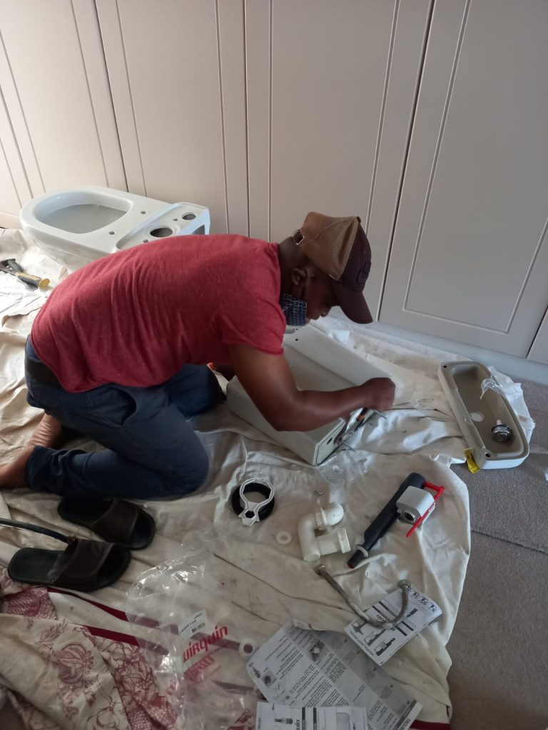 Plumber fitting a basin on a dust sheet — emergency plumber cape town