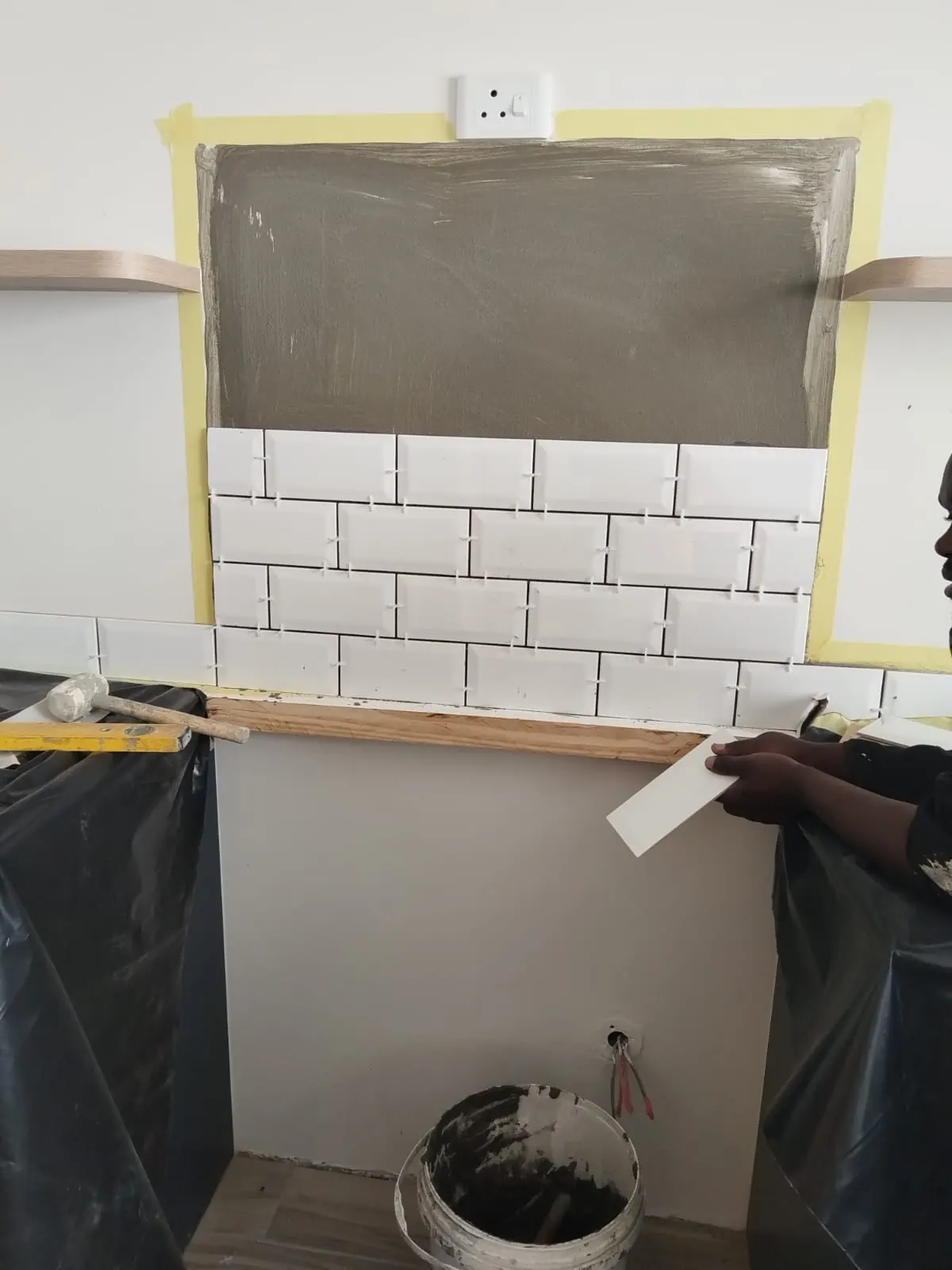 Subway-tile splashback being installed over taped adhesive bed