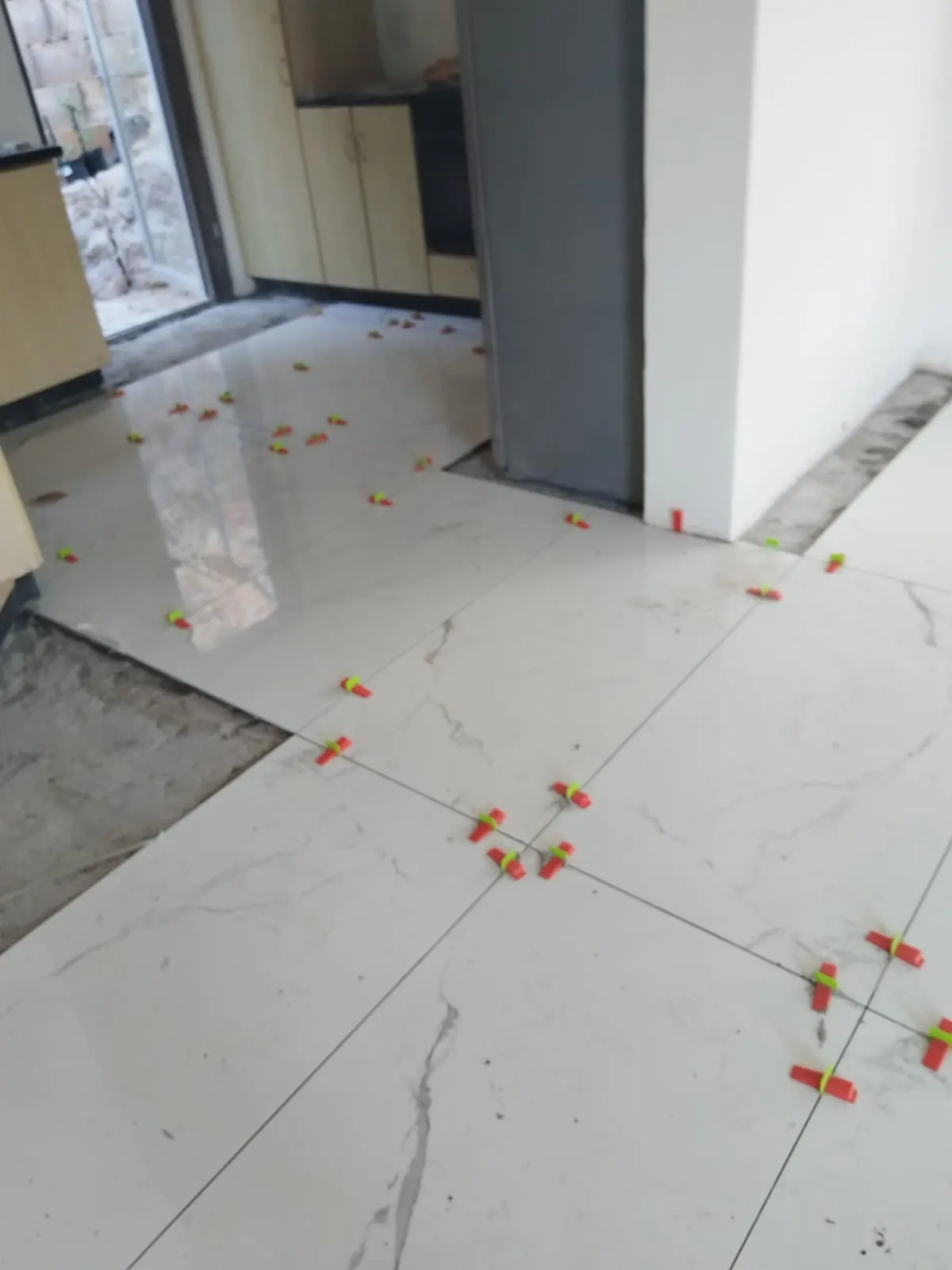 Polished marble-look floor tiles with levelling clips at a doorway
